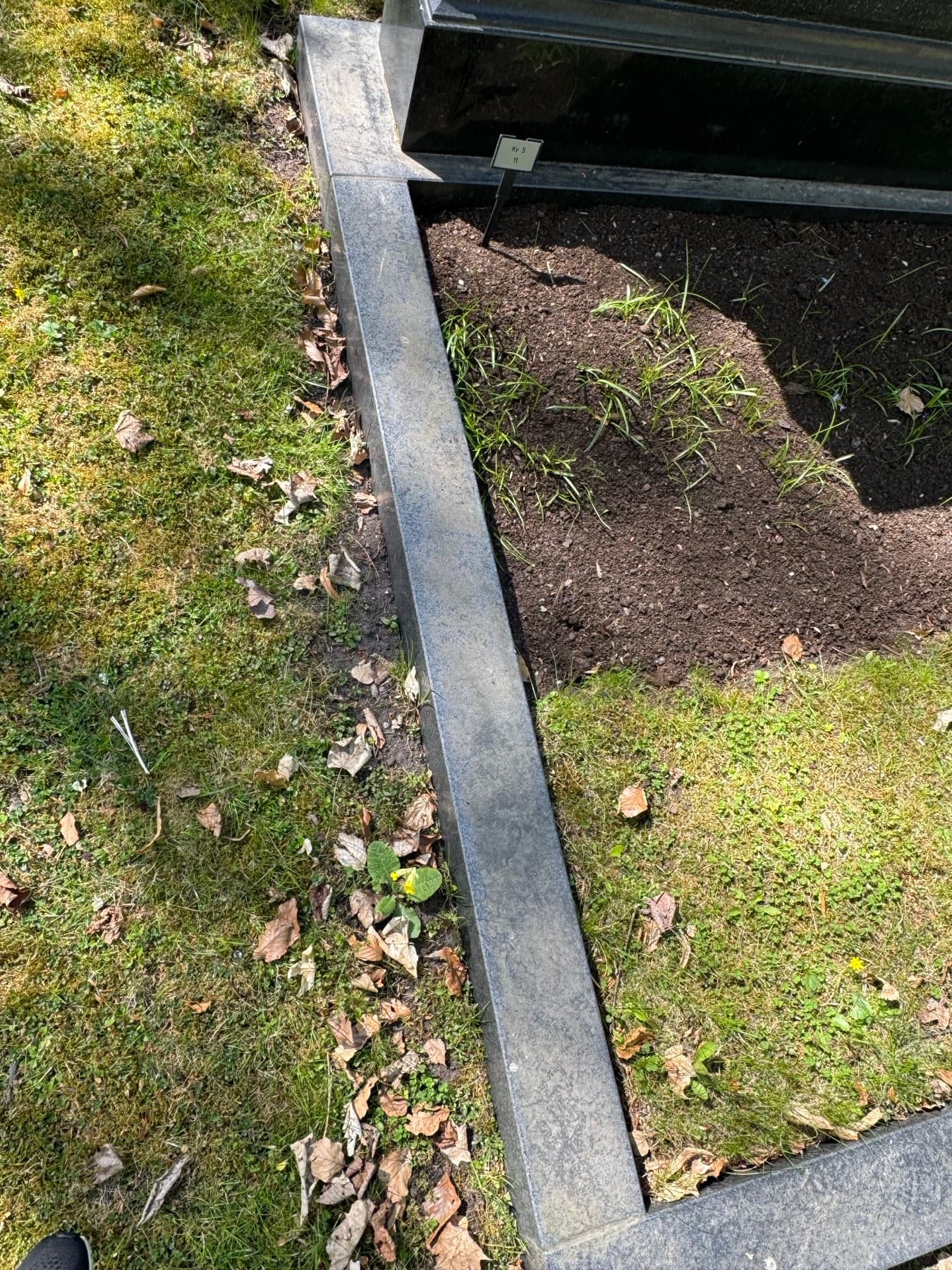 Stenramen runt graven före tvätt – jord och gräs över kanten