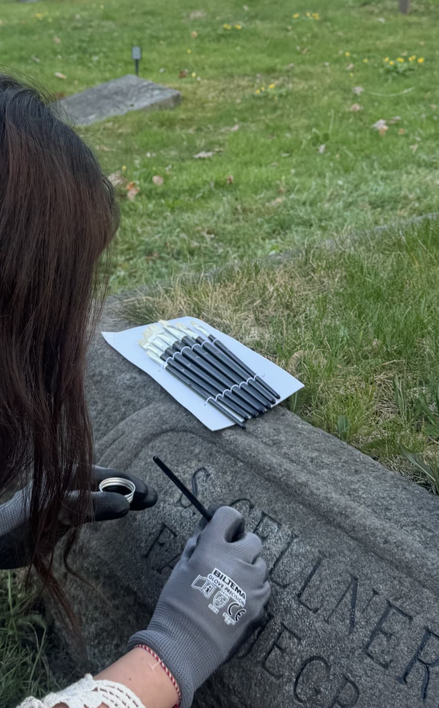Minnesfrid fyller i bokstäver på en gravsten med tunn pensel och skyddshandskar